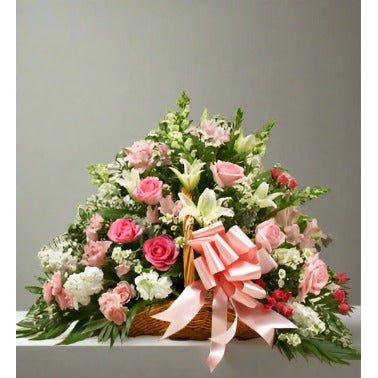 Pink and white flowers in a fireside basket with a pink ribbon on the side.