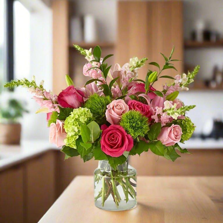 A bouquet of pink and green flowers in a glass vase on a kitchen counter.