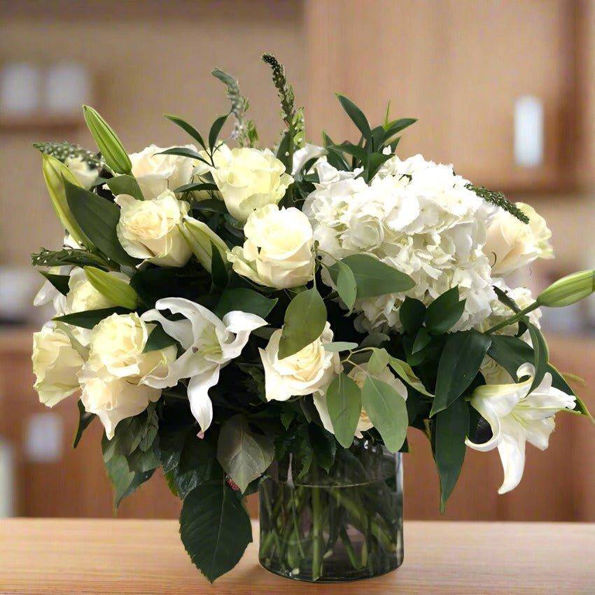 white floral arrangement in a clear cylinder vase with roses and lilies.