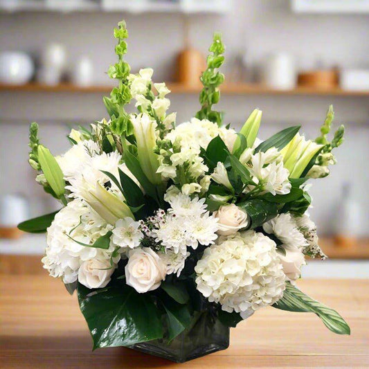 A luxury arrangement in a big square vase with all white lilies, roses, hydrangeas pomp's and fillers.
