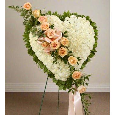 White Heart Tribute  A heart shape standing sympathy arrangement with peach roses across the heart and standing on an easel  