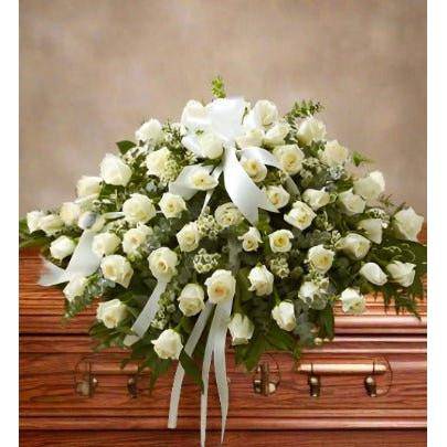 White roses with greens set on the wooden casket .