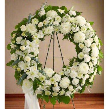 White Standing Wreath with all white flowers and green leaf's with a white ribbon on the side.