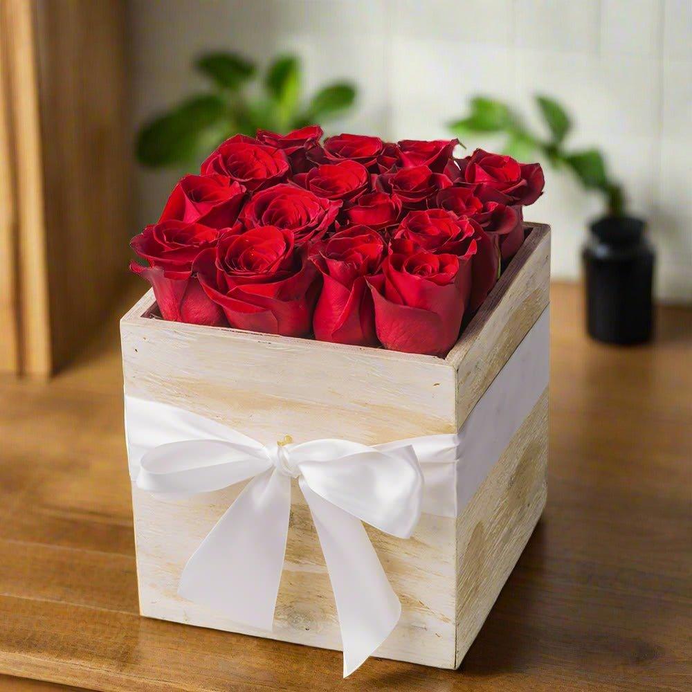 Square wooden box filled with red roses, tied with a white ribbon.